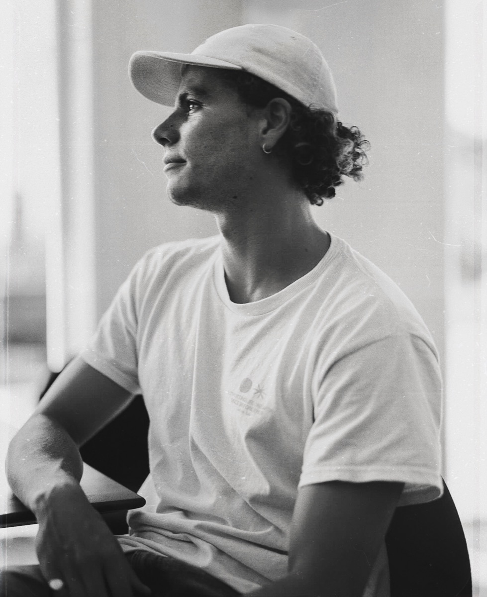 Rhys Warren, seated portrait in a cap and white tee